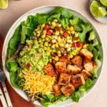 Copycat chipotle chicken in bowl with greens, corn salsa, guacamole and cheese.