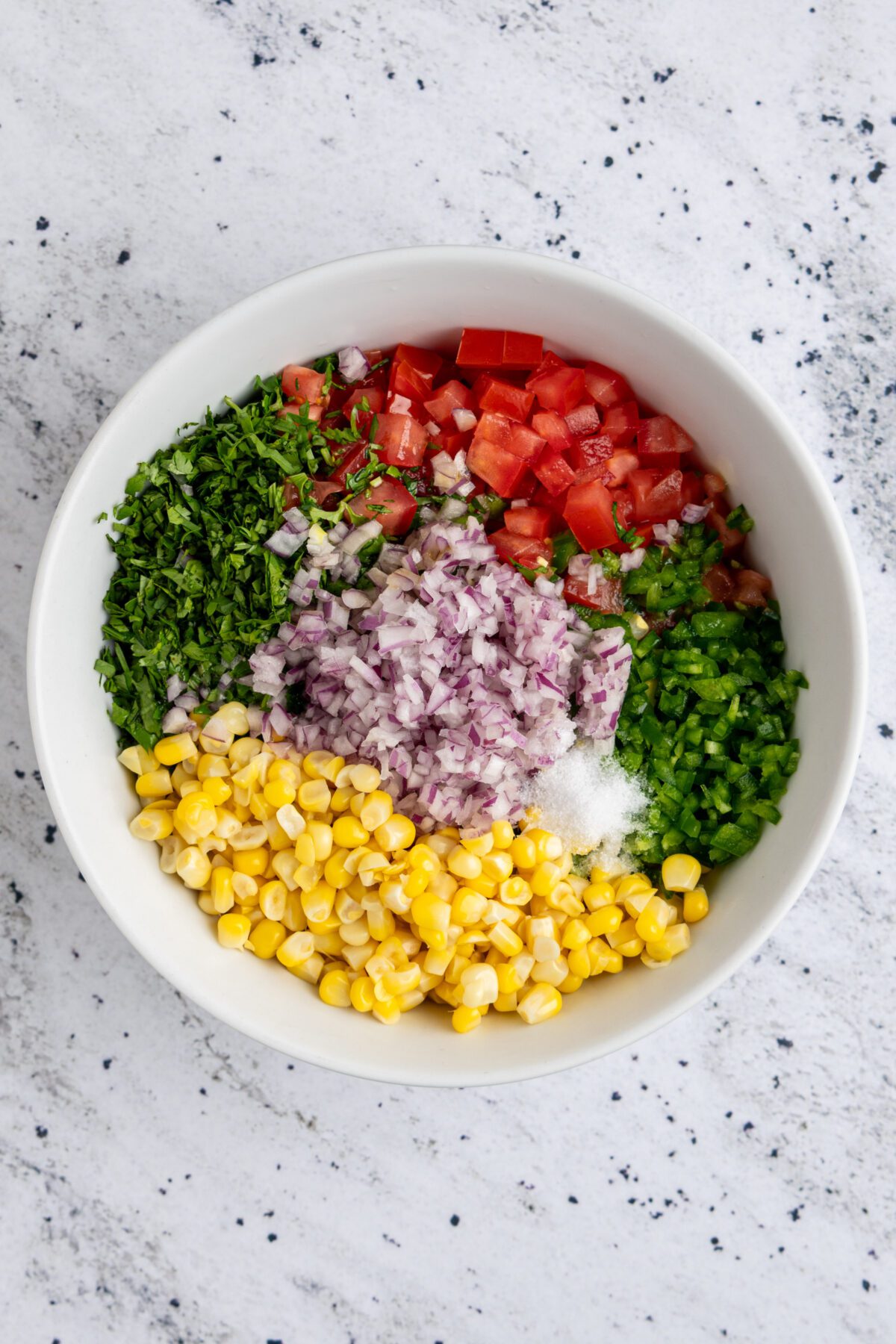 corn, tomatoes, onion, cilantro, jalapeño, lime juice, lemon juice, vegetable oil, and salt in white bowl