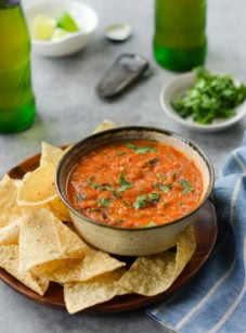 Bowl of roasted tomato salsa on a plate with chips.