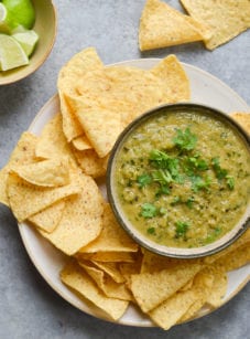 Bowl of salsa verde on a plate with tortilla chips.