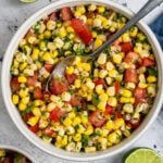 corn salsa in white bowl with limes and spoon next to bowl