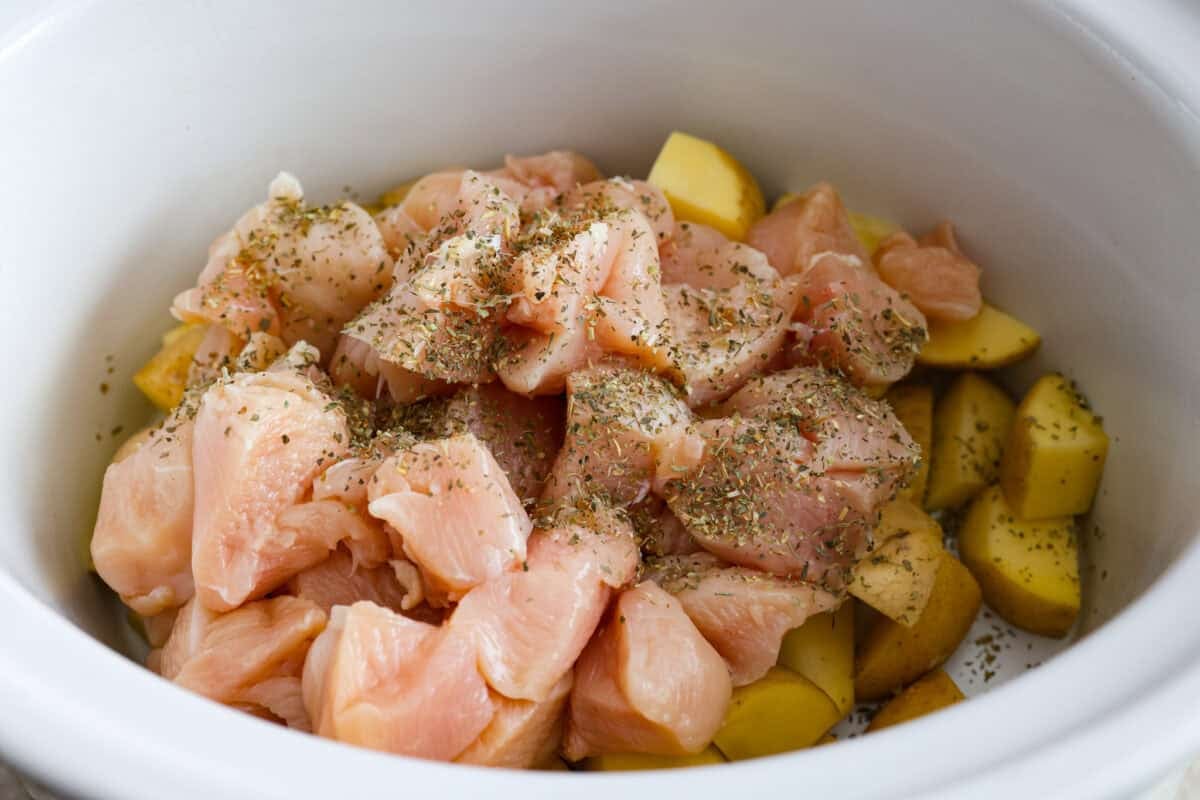 Cubed chicken with Italian seasoning placed on top of the potatoes in the slow cooker.  