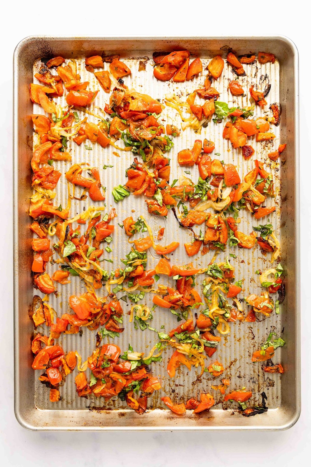 baking sheet with cooked tomatoes and onions sprinkled with fresh basil