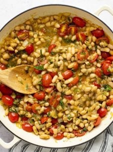 ragout with wood spoon in dutch oven sitting on a striped napkin with small container of salt to the side