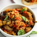 white bowl with caponata with baguette slices topped with caponata nearby