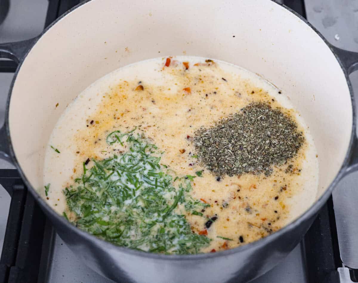 Angle shot of the cream, broth, basil and seasonings added to the pot to make the marry me ramen broth.