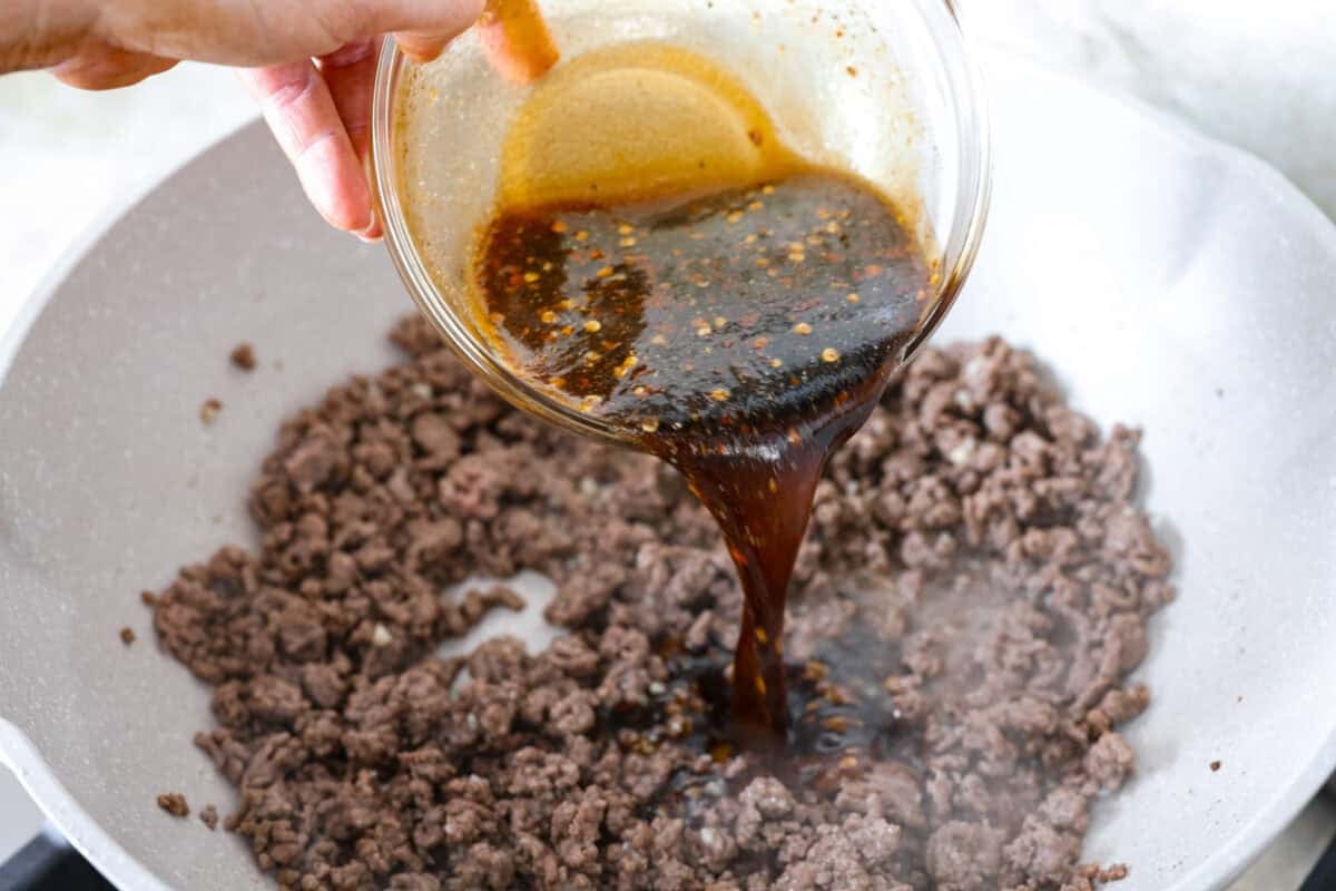 Someone pouring the sauce into the cooked ground beef.