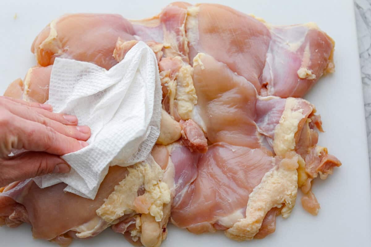 Apple cider chicken thighs bring all the best fall flavors to your plate! Juicy chicken, caramelized apples, and a rich cider sauce for the ultimate cozy dinner. Someone dabbing the chicken thighs dry with a paper towel.