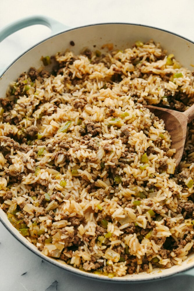 Dirty rice with meat and veggies being served with a wooden spoon.