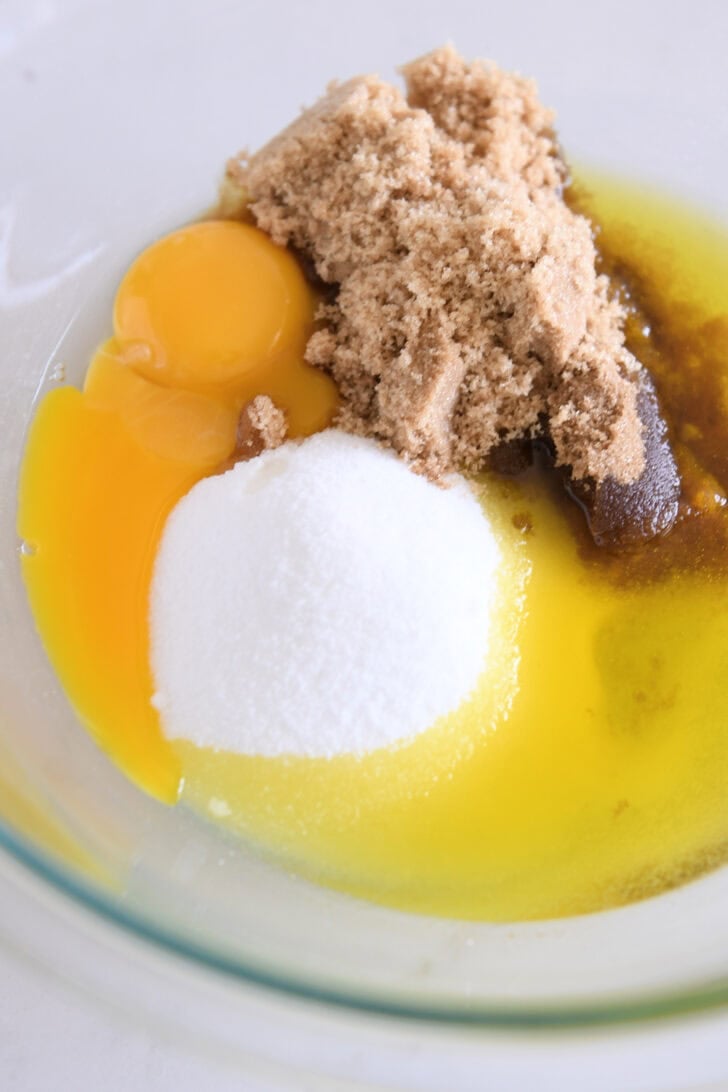 Glass bowl with eggs, brown sugar, olive oil and granulated sugar.