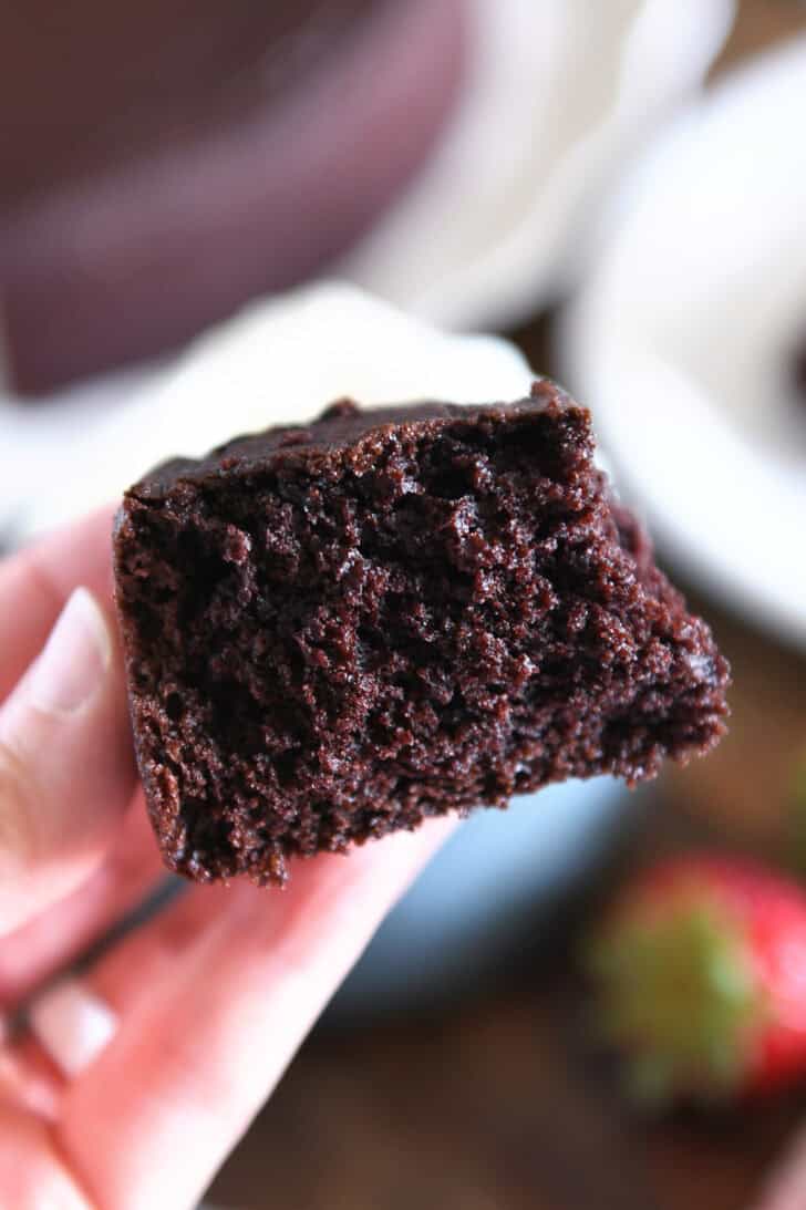 Holding half piece of chocolate olive oil cake in fingers.