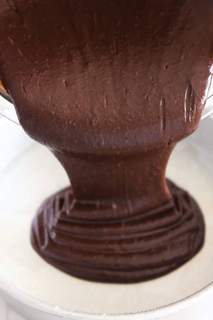 Pouring chocolate cake batter in parchment lined cake pan.