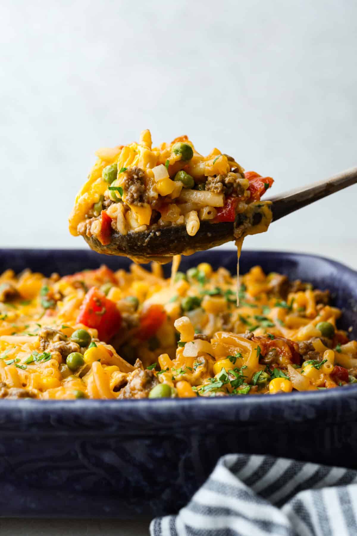 Side shot of someone lifting a scoop of shipwreck casserole from the baking dish.
