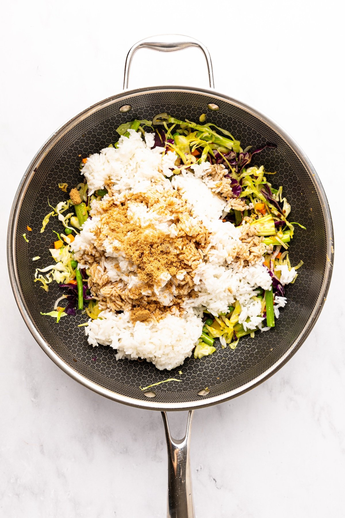 nonstick skillet with rice, soy sauce, fish sauce, and brown sugar  piled on top of veggie/aromatic mixture