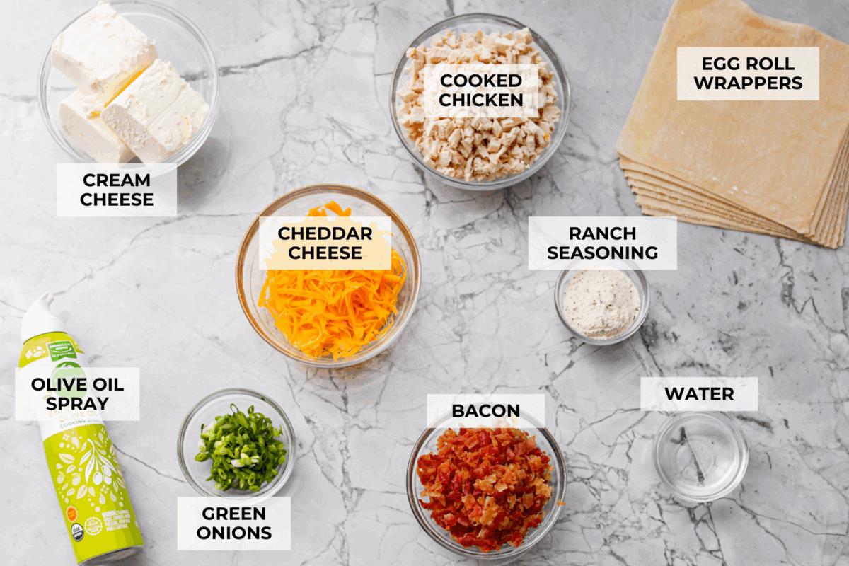 Crack Chicken Egg Rolls wrap savory chicken, crispy bacon, melty cheese, and zesty ranch in a golden, crunchy shell. Easy to make, lighter than deep-fried versions, and perfect for parties or game day! Overhead shot of labeled ingredients.
