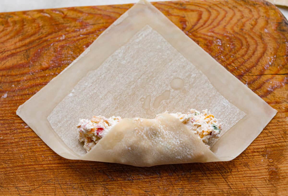 Crack Chicken Egg Rolls wrap savory chicken, crispy bacon, melty cheese, and zesty ranch in a golden, crunchy shell. Easy to make, lighter than deep-fried versions, and perfect for parties or game day! Egg roll wrapper with water lining the edges, and one corner wrapping around the filling.