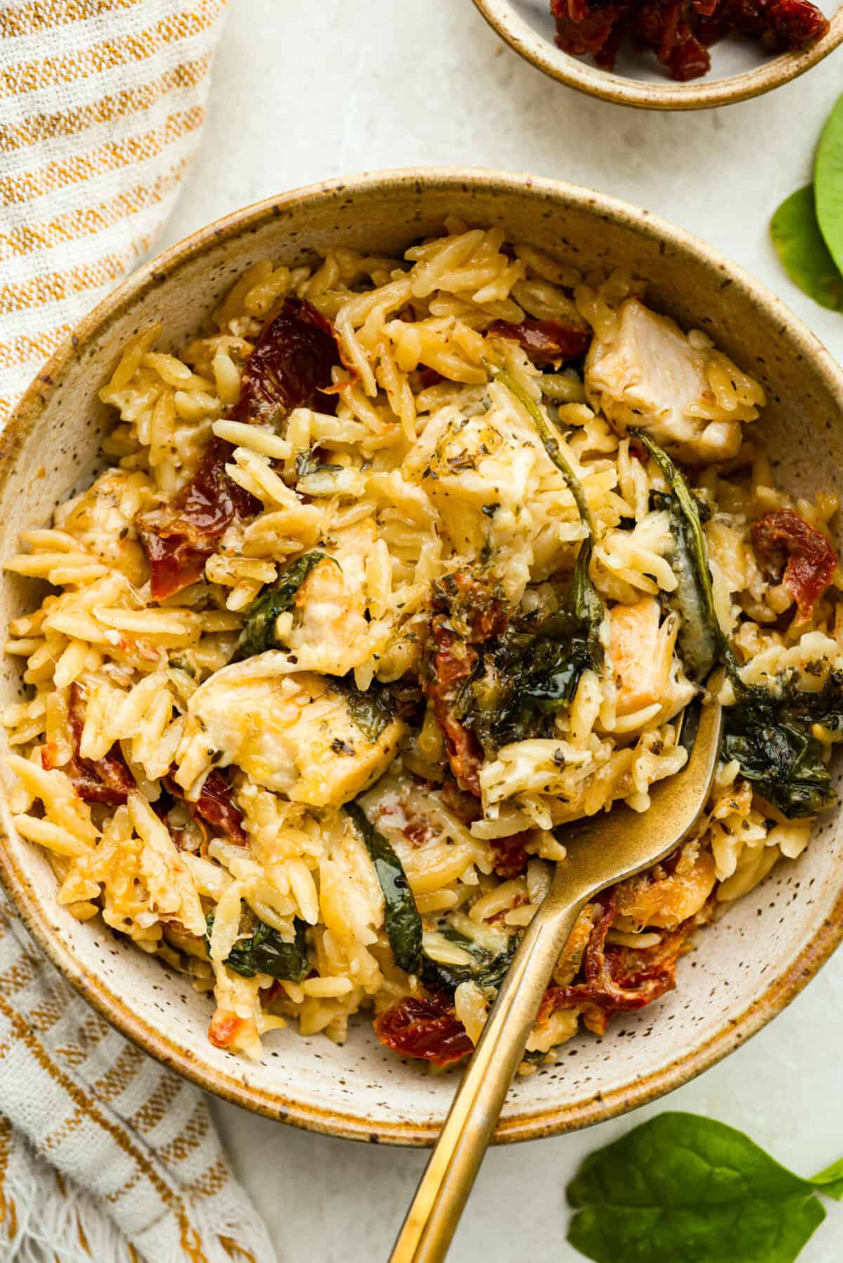 Bowl of tuscan chicken orzo bake with a gold fork.