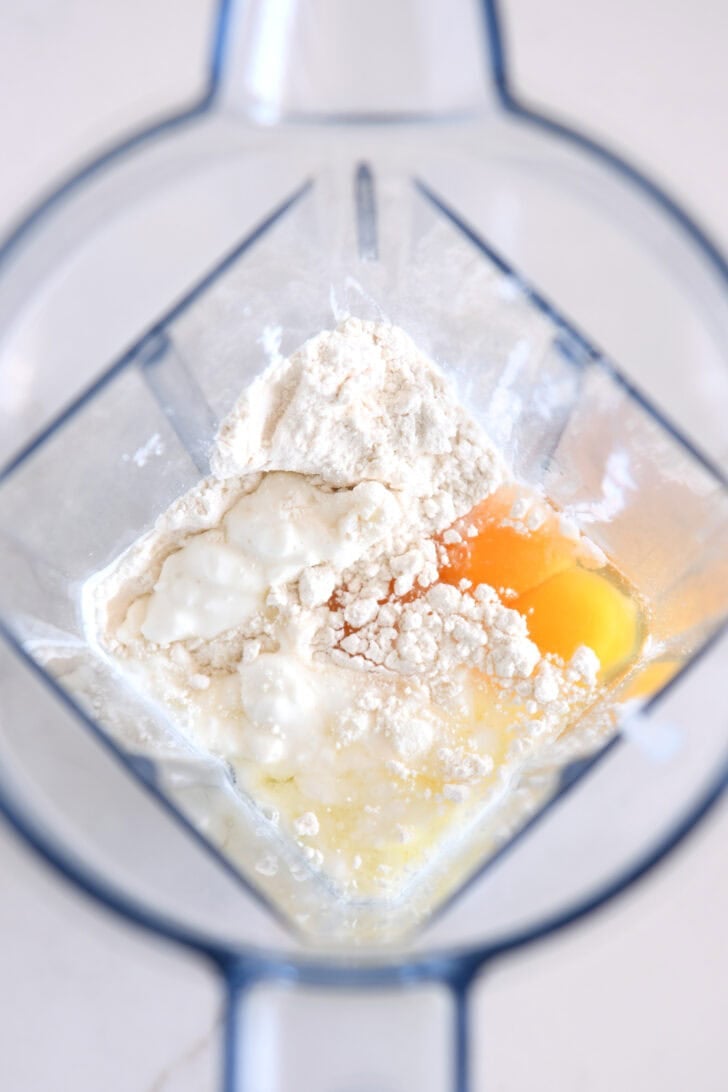 Top down view of blender with cottage cheese, flour, eggs, baking powder and salt.