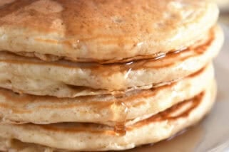 Stack of four pancakes on white plates with syrup drizzled down the side.
