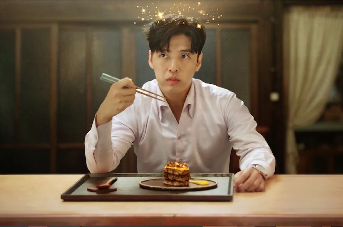 A man in a pale lavender-pink button-down shirt sits at a lunch counter holding chopsticks poised in front of his face. He's just eaten a bite of an artfully crafted dish in front of him, and judging by the cartoon stars haloing his head, his mind has been blown