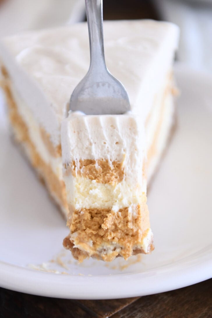 Slice of pumpkin swirl cheesecake with bite removed on white plate.