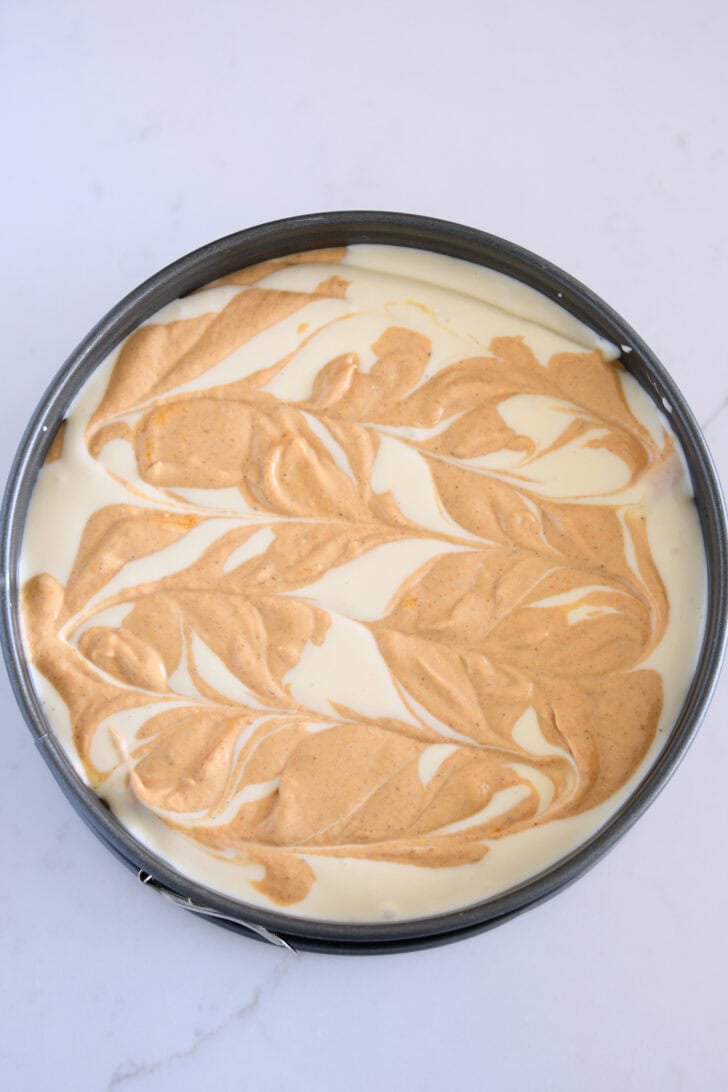 Top down view of pumpkin cheesecake batter swirled into regular cheesecake batter in 9-inch springform pan.