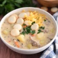 Soup bowl with sausage potato soup topped with oyster saltine crackers, fresh parsley and grated cheese.