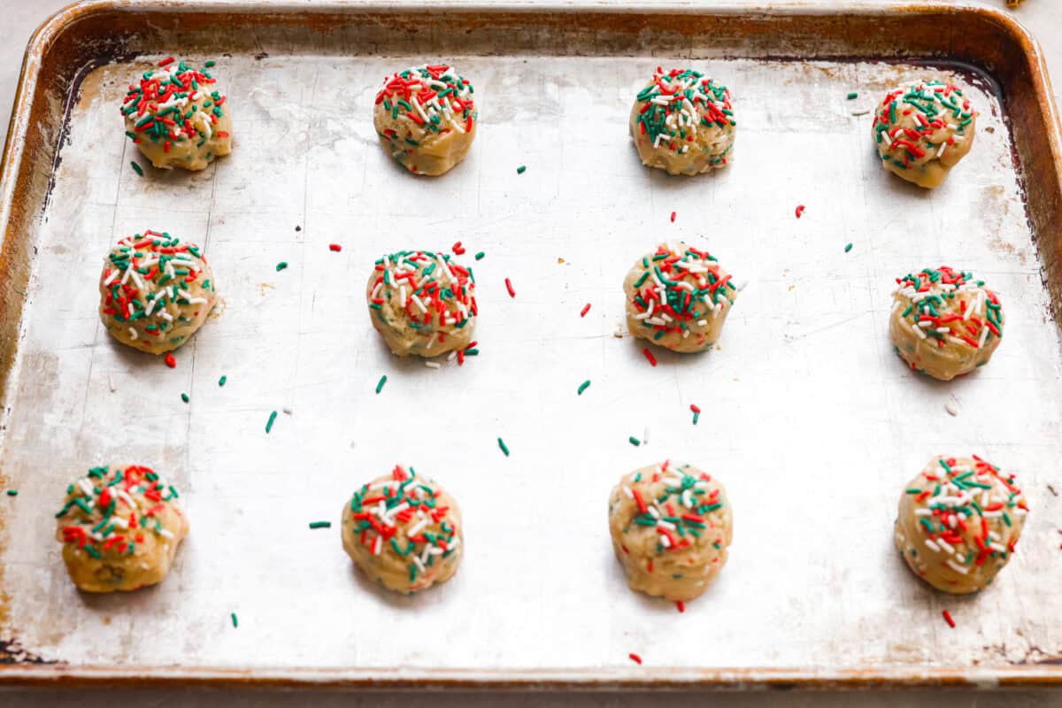 Balls of cookie dough with extra sprinkles added on top, evenly spread out on a cookie sheet. 