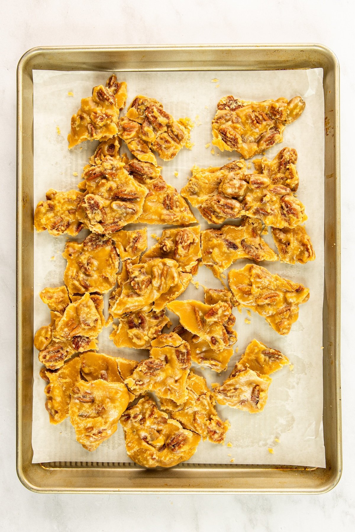 parchment-lined baking sheet with cooled pralines broken into pieces