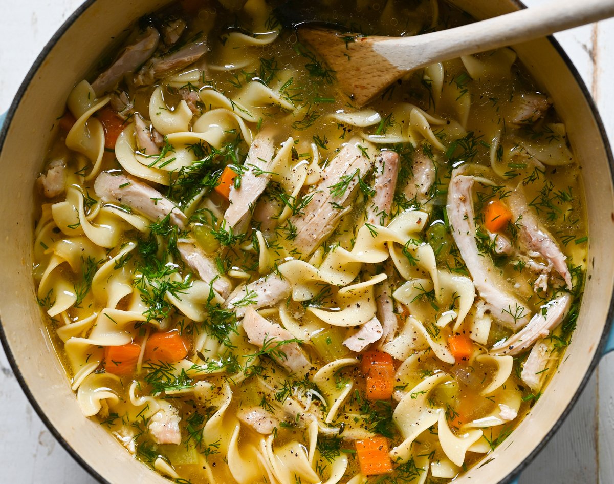 chicken noodle soup in pot with wooden spoon.