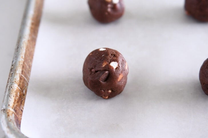 Chocolate cookie dough ball with mini marshmallow bits on parchment-lined baking tray.