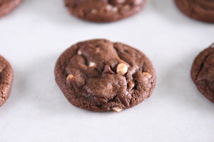 Baked hot cocoa chocolate cookie with mini marshmallow bits on parchment-lined baking tray.