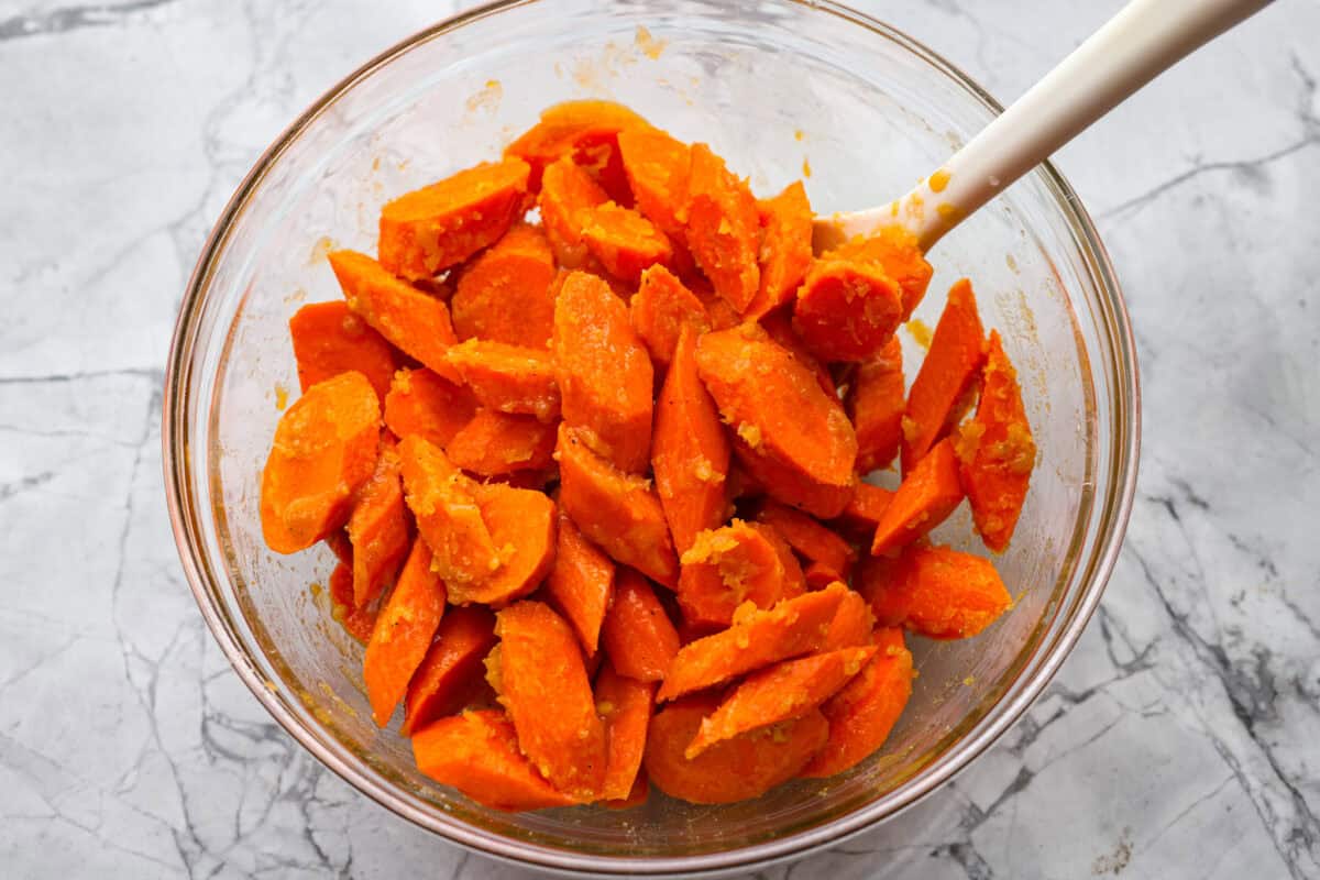 Someone stirring the sliced carrots with the glaze. 