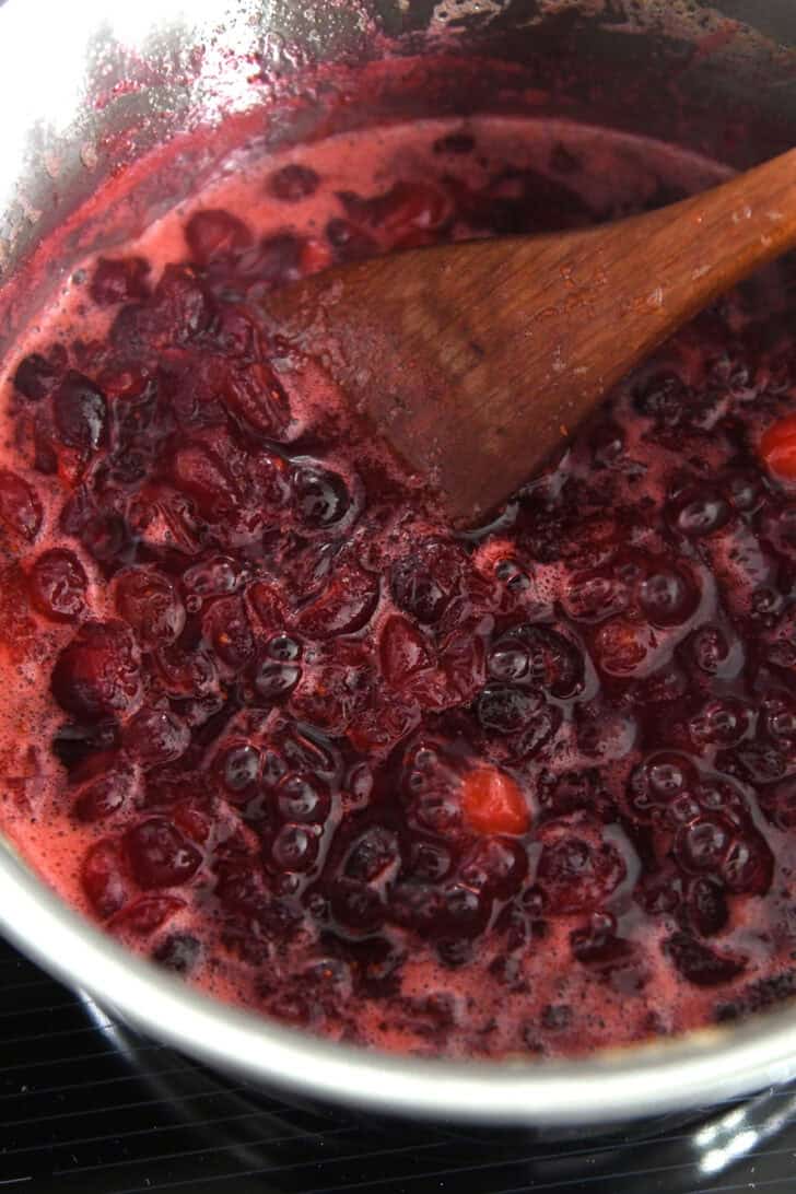 Saucepan with thick, simmered mixture of fresh cranberries, orange juice and sugar.