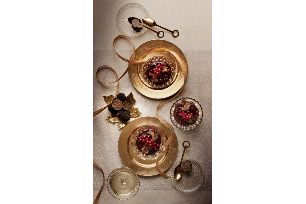 Gourmet still life featuring black truffles, red berries, gold plates, and spoons. Urbani Tartufi.