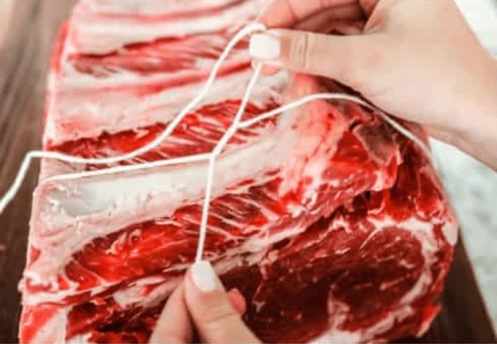 Someone tying the prime rib with butchers twine.