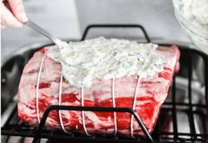 Someone spreading the garlic herb butter on top of the prime rib roast.