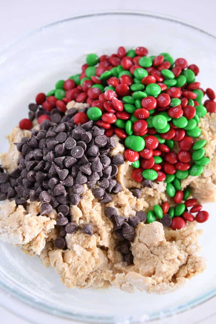 Glass bowl with cookie batter, chocolate chips and red and green M&Ms.