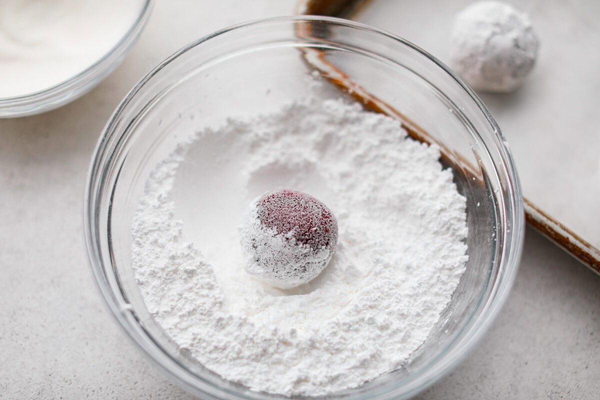 A cookie dough ball in a bowl of powered sugar.