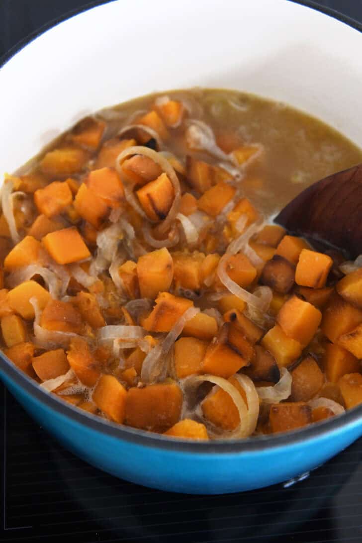 Soup pot with wooden spoon stirring broth, butternut squash pieces, onions and broth.