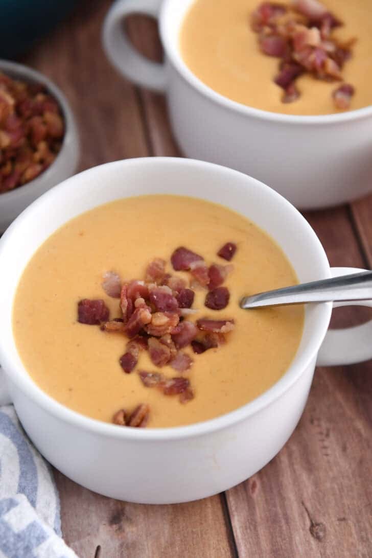 Two white bowls with butternut squash soup topped with cooked and crumbled bacon.