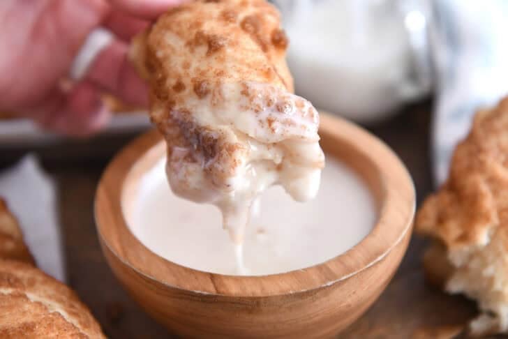 Dipping cinnamon sugar twist in bowl of sweet icing.
