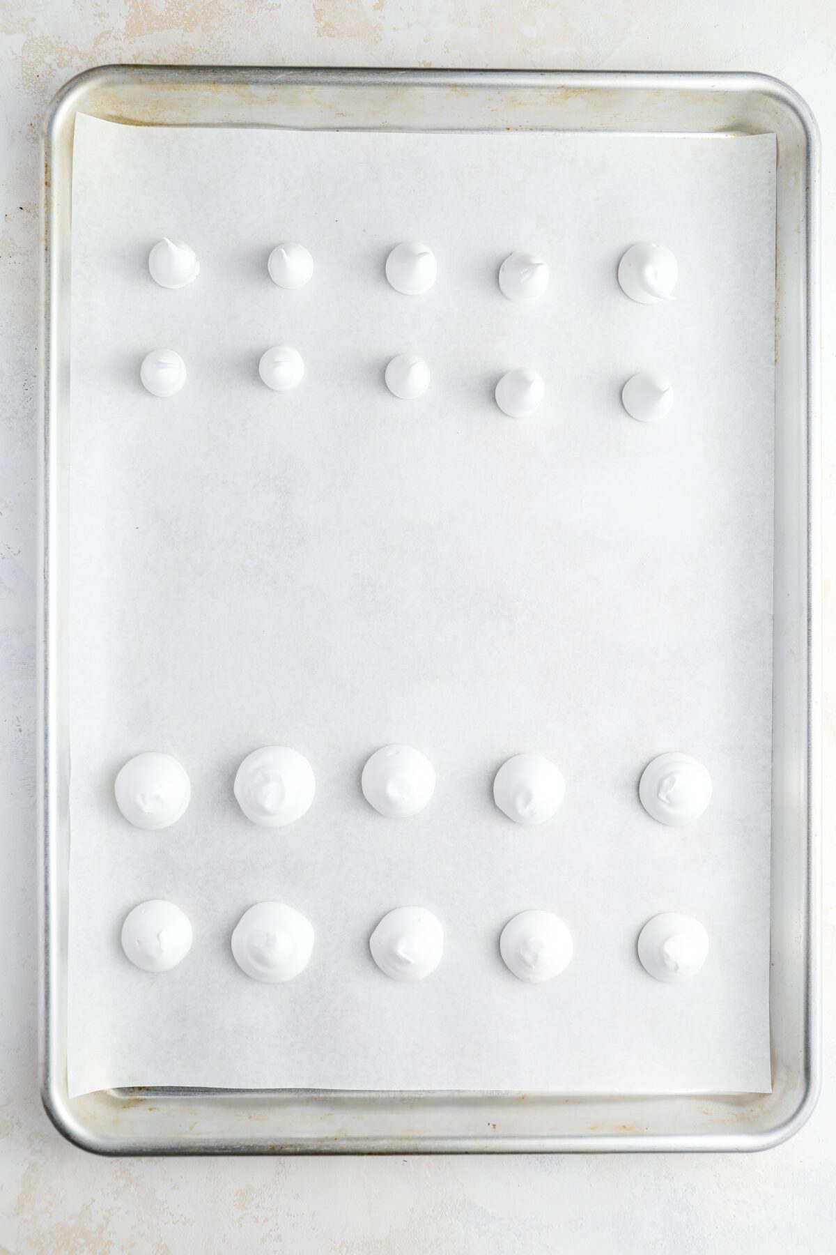 parchment-lined baking sheet with unbaked meringue mushroom caps and stems