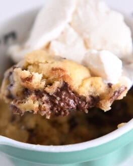Spoon scooping up bite of warm chocolate cookie in mug with ice cream.