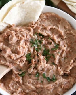 Top down view of white bowl with easy refried beans, cilantro and tortillas.