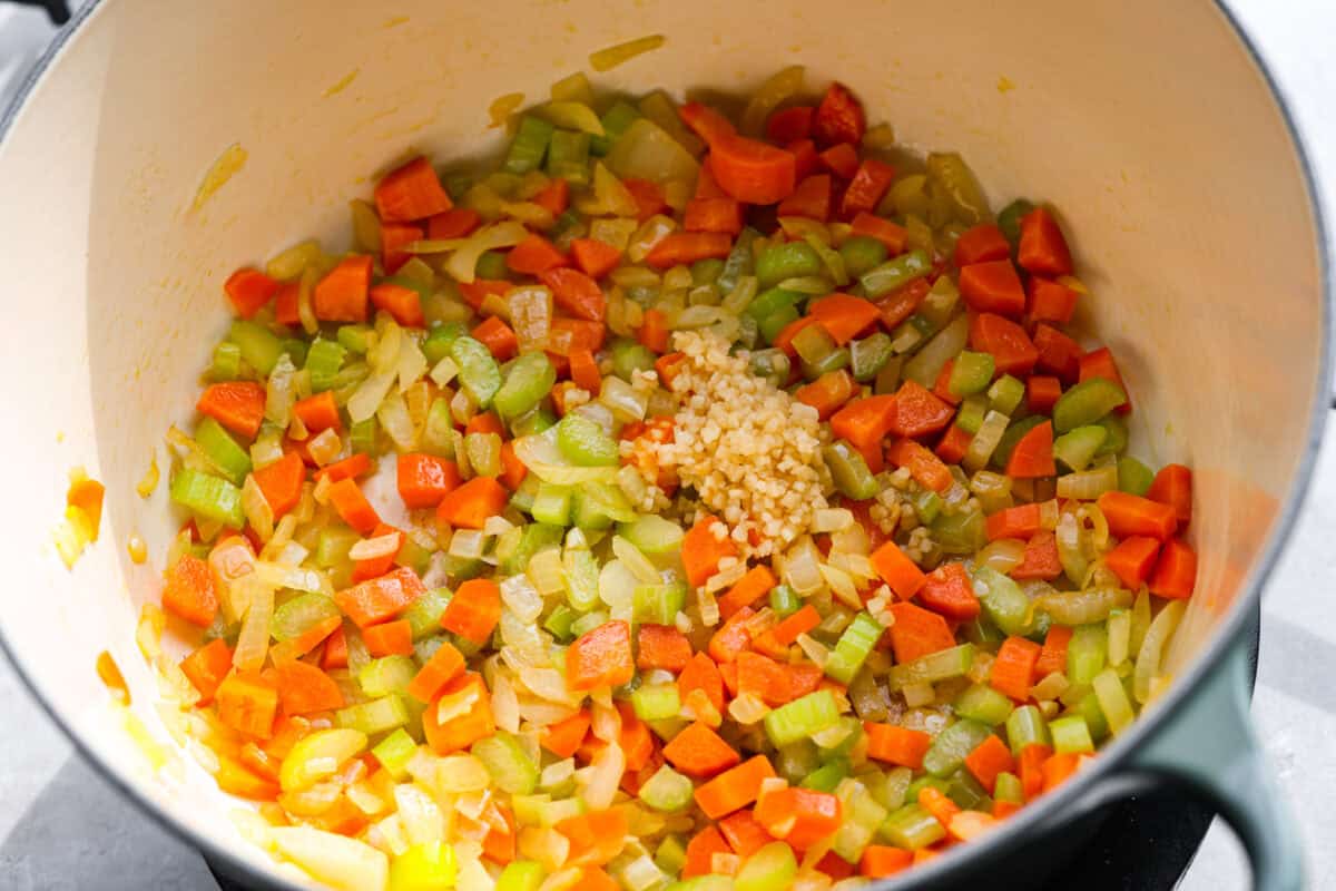 Celery, carrots, and onion cooking in a pot, with garlic added to it. 
