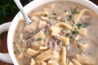 Spoon scooping up bite of thick noodles, broth and ground beef.
