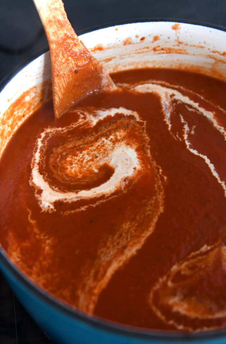 Cast iron enamel pot with homemade tomato soup and swirls of heavy cream.