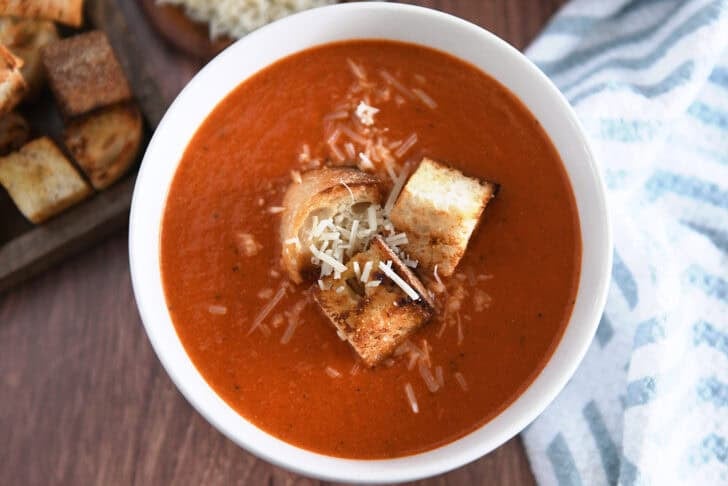 Top down view of white bowl filled with homemade tomato soup, homemade croutons and parmesan cheese.