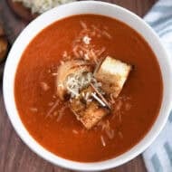 Top down view of white bowl filled with homemade tomato soup, homemade croutons and parmesan cheese.